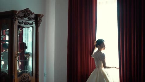 Bride Standing by Window in White Wedding Dress