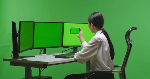 Woman Using Mobile Phone And Multiple Computer Monitor With Mock Up Green Screen In Green Screen