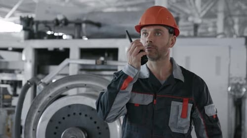 Focused Man Speaks Into Walkie Talkie in Factory