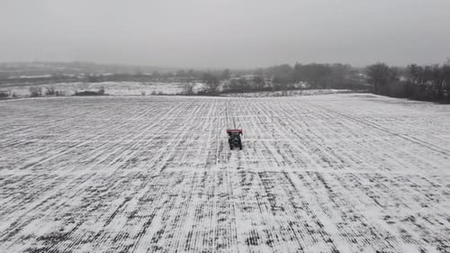 Tracteur épandant des engrais et des pesticides en hiver sur un champ de neige