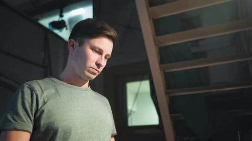 Man Standing Thoughtfully in Dim Studio Near Industrial Staircase