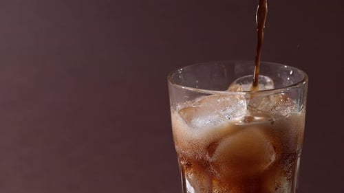 Pouring cola drink with ice cubes close-up.