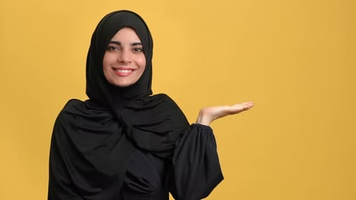 Beauty Muslim Woman in Black Hijab Pointing Hand Copy Space Advertising Posing Isolated on Orange