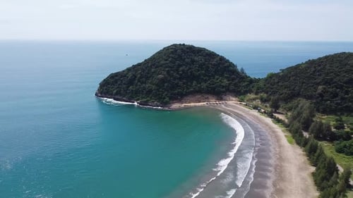 Aerial view of tropical beach and turquoise sea water with small waves close to green mountains.