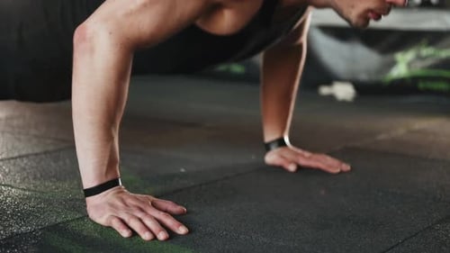 Young sportive strong man in black wear doing push-ups in gym
