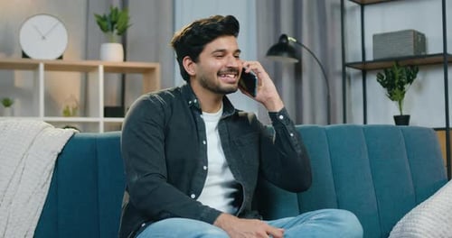 Smiling Man Chatting on Smartphone on Blue Couch