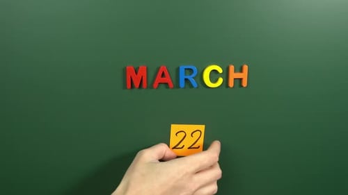 Hand sticking a sticker 22 March calendar day on school board. 22 date of March. Twenty second day