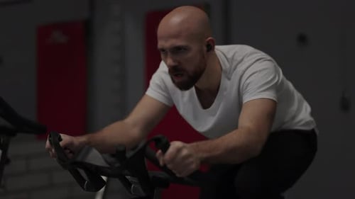 Bald Man Exercising on a Stationary Bike in the Gym