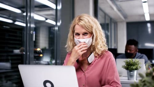 Mature businesswoman wearing face mask working late in office during coronavirus pandemic