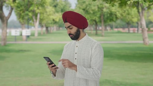 Serious Sikh Indian man using phone in park