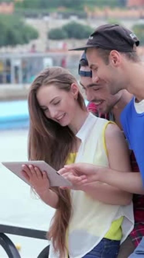 Friends Enjoy Using Tablet Device Outdoors Near City River