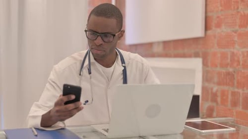Doctor Using Phone and Laptop in Bright Office