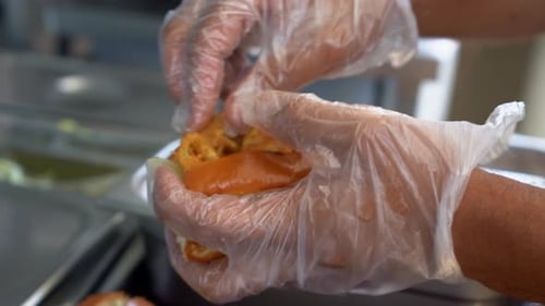 A chief puts chicken pieces in a sandwich, close up shot, insert shot