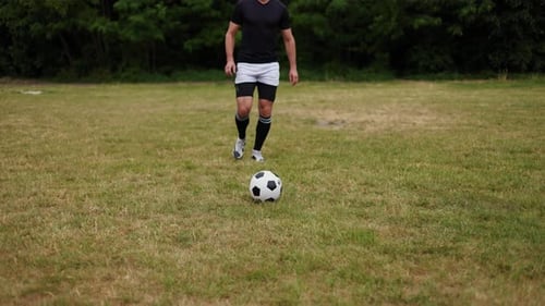 Sporty Male Running on Field with Classic Black and White Soccer Ball at Feet