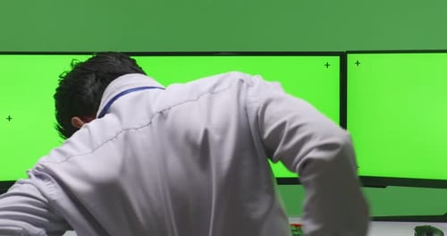 Hombre con dolor de espalda mientras trabajaba con una maqueta de monitor de computadora múltiple en un estudio de pantalla verde