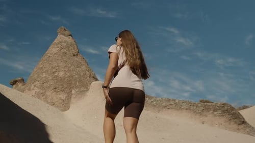 Eine junge Frau schlendert durch uralte Sandhügel, von hinten gesehen, unter strahlend blauem Himmel.