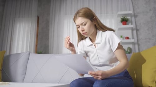 Sad woman looking at papers in her hand. Bad news.