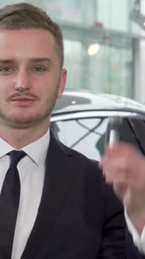 Confident Car Salesman Showcasing Keys in a Sleek Dealership
