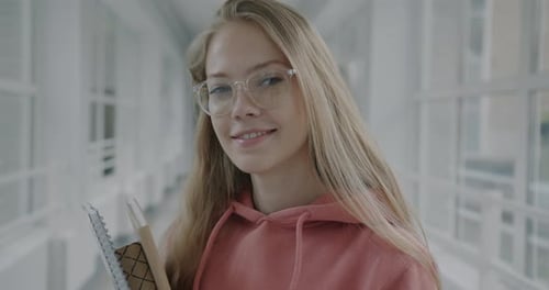 Portrait of Intelligent Young Lady Wearing Glasses Standing in High School Hallway Holding Books