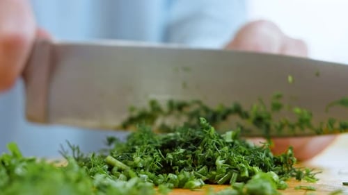 a Woman's Hand Cuts Green Onions with a Knife on a Wooden Chopping Board