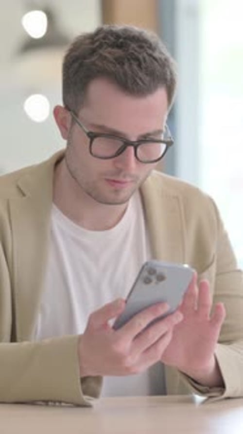 Young Man Using a Smartphone Indoors at a Table