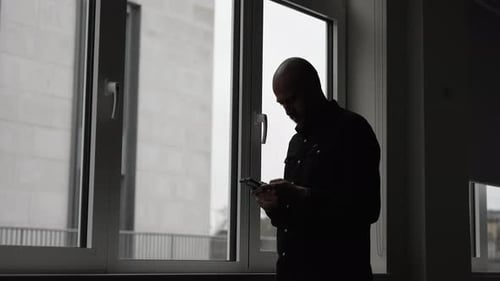Bald Man Using Phone in Dark Room Silhouette