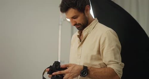 Side View of a Confident Guy a Brunette Cameraman with a Beard in a White Shirt Examines the