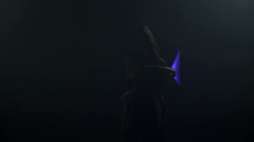 Young Man in Jedi Cosplay Costume with Lightsaber Battle on Black Background in Smoke and Rain Slow