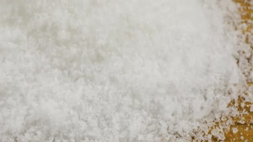 Fine crystals of natural sea salt fall onto a wooden surface. A big pile of salt, lots of salt.