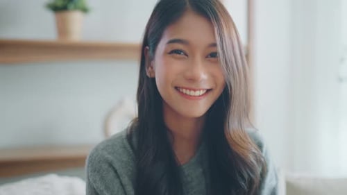 Confident smiling young adult asian woman looking at camera while sitting at home