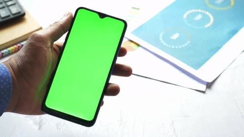 Phone with Green Screen Held Above a Desk