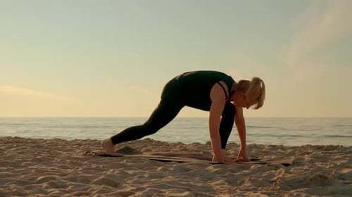 Attractive Woman Wearing Sportswear Doing Stretching Yoga Exercises on Fitness Mat at Sunset Beach