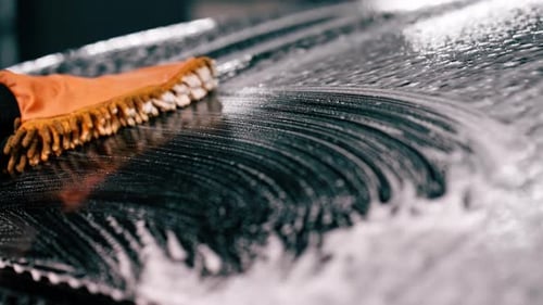 Close-up of a car wash worker using a microfiber cloth to wash black luxury car with car wash