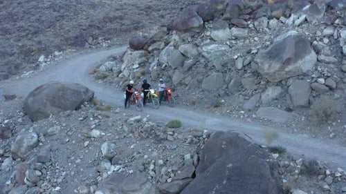 Three motocross bikers standing in row on gravel road. Aerial circling shot.