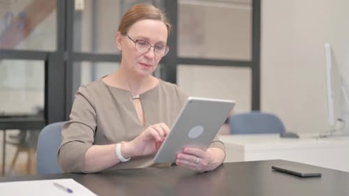 Old Businesswoman Doing Video Chat on Tablet in Office