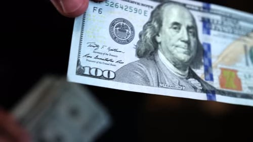 One hundred dollar bill close-up held by a man's hand and twirls teasing the camera.