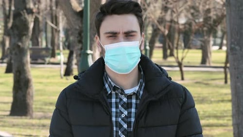 Young Man Standing in City Park in Protective Medical Mask