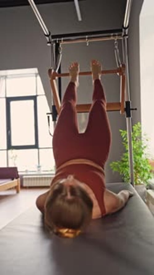 Woman Doing Pilates Exercises on Balanced Body Cadillac Machine at Studio Focusing on Strength and