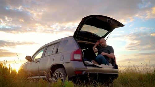 Homem de negócios cansado trabalha duro em um laptop respirando profundamente sentado no porta-malas do carro enquanto