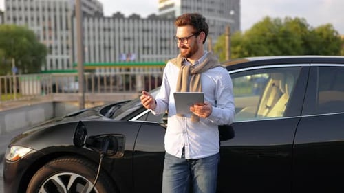 Bearded Man with Tablet at Electric Vehicle