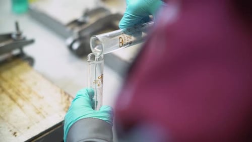 Closeup Backside Lab Worker Fills Beaker with Clear Liquid