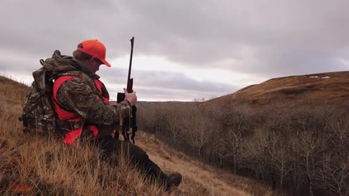 Hunter on Hillside Adjusting his Hunting Rifle