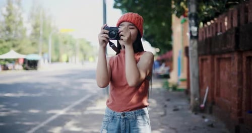 An Asian woman stands holding a camera to take pictures of the city view on the sidewalk.