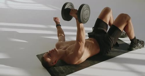 Man Lying on Mat Lifting a Dumbbell