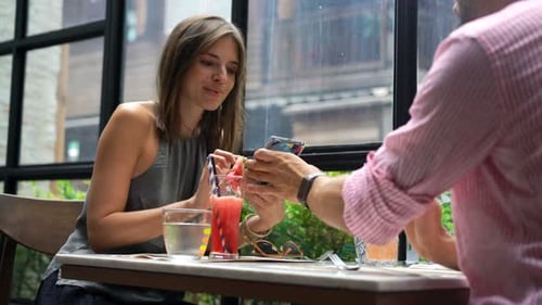 Young couple in city cafe chatting and touching smartphone screen on date