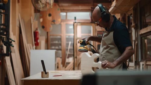 Luthier Sanding a Guitar Body with a Power Sander in His Woodworking Workshop