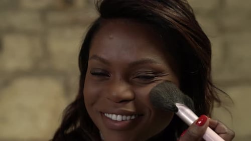 Close up black girl smiling in the camera applying makeup, powdering brush.