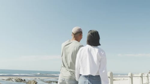 Happy biracial couple walking together and holding hands on promenade, in slow motion