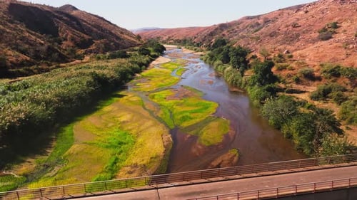 Aerial View Moving Towards a Bridge Over a River with Lush Green Vegetation on Its Banks Surrounded