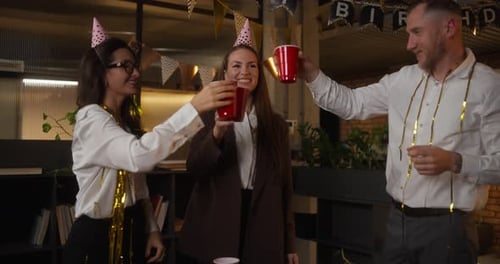 Um trio de trabalhadores de escritório em roupas de negócios levanta copos de plástico e tilinta os óculos durante uma